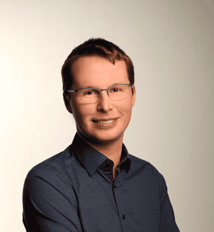 Junger Mann mit Brille und Hemd vor neutralem Hintergrund.