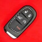 Remote car key fob with lock, unlock, trunk, and panic buttons on red background.