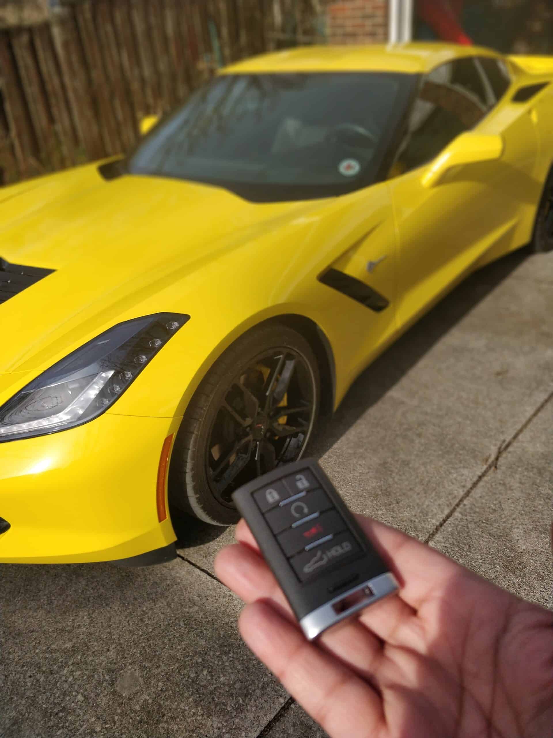 Yellow sports car with remote key fob in front of it, parked outdoors.