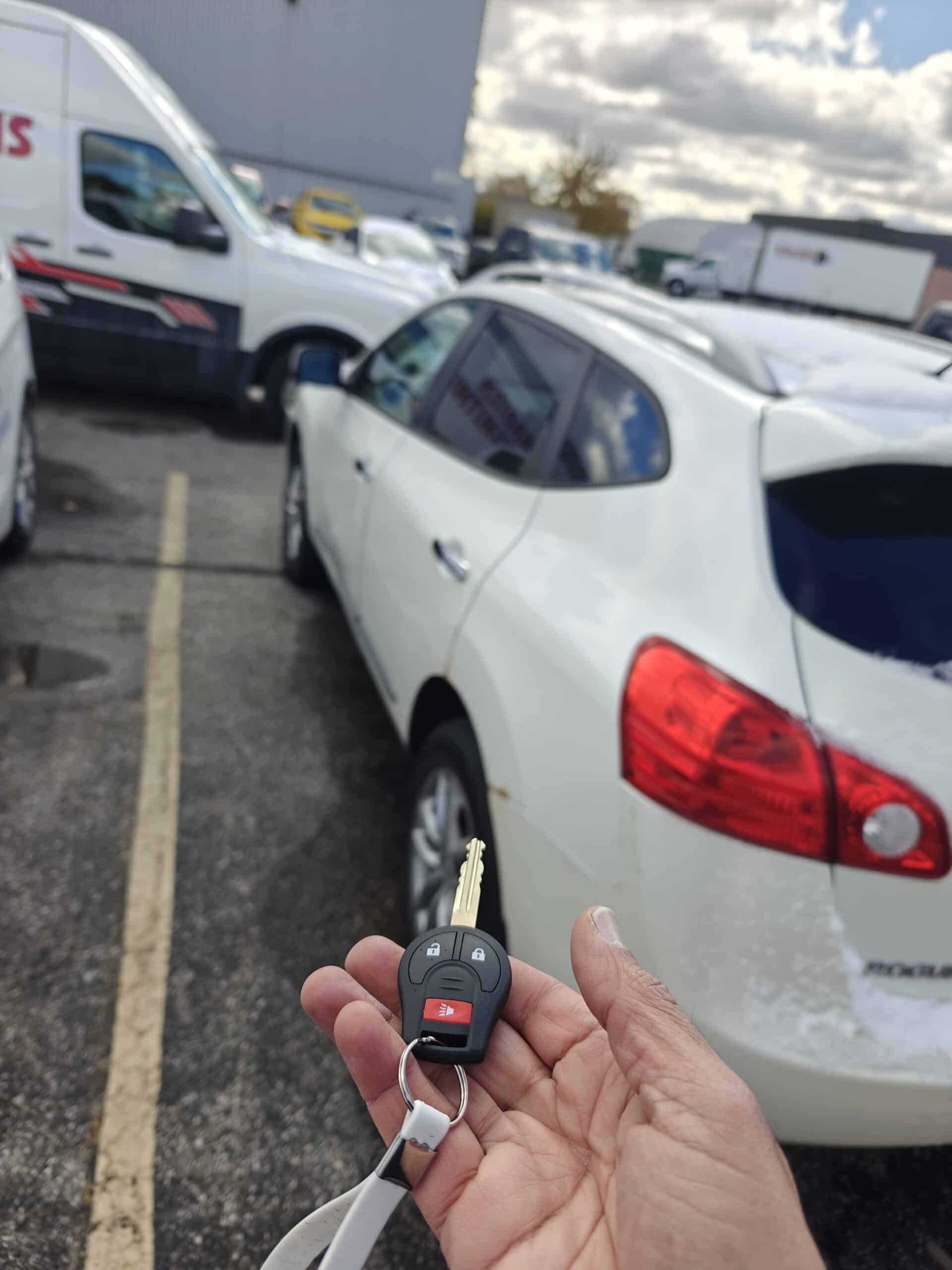 Key fob with keys in hand near white car parked in lot, showcasing locksmith services.