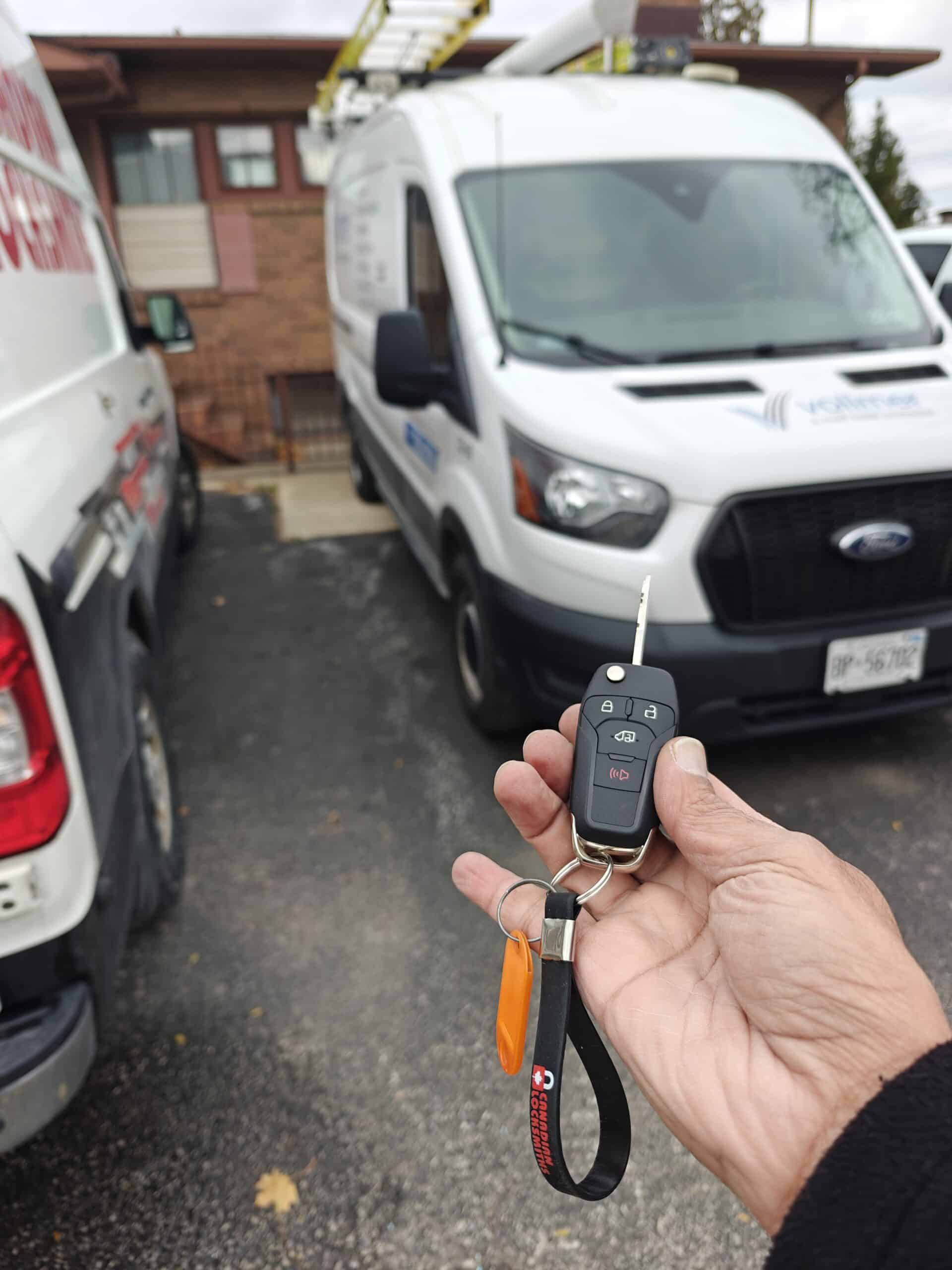 Remote car key in hand with service van in background, illustrating locksmith services in Windsor.