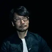 Man wearing glasses and a black jacket, looking thoughtfully into the distance.