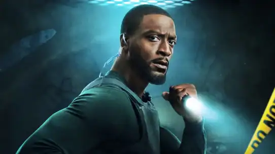 Suspenseful man holding flashlight, wearing tactical gear, in a dark, tense environment.