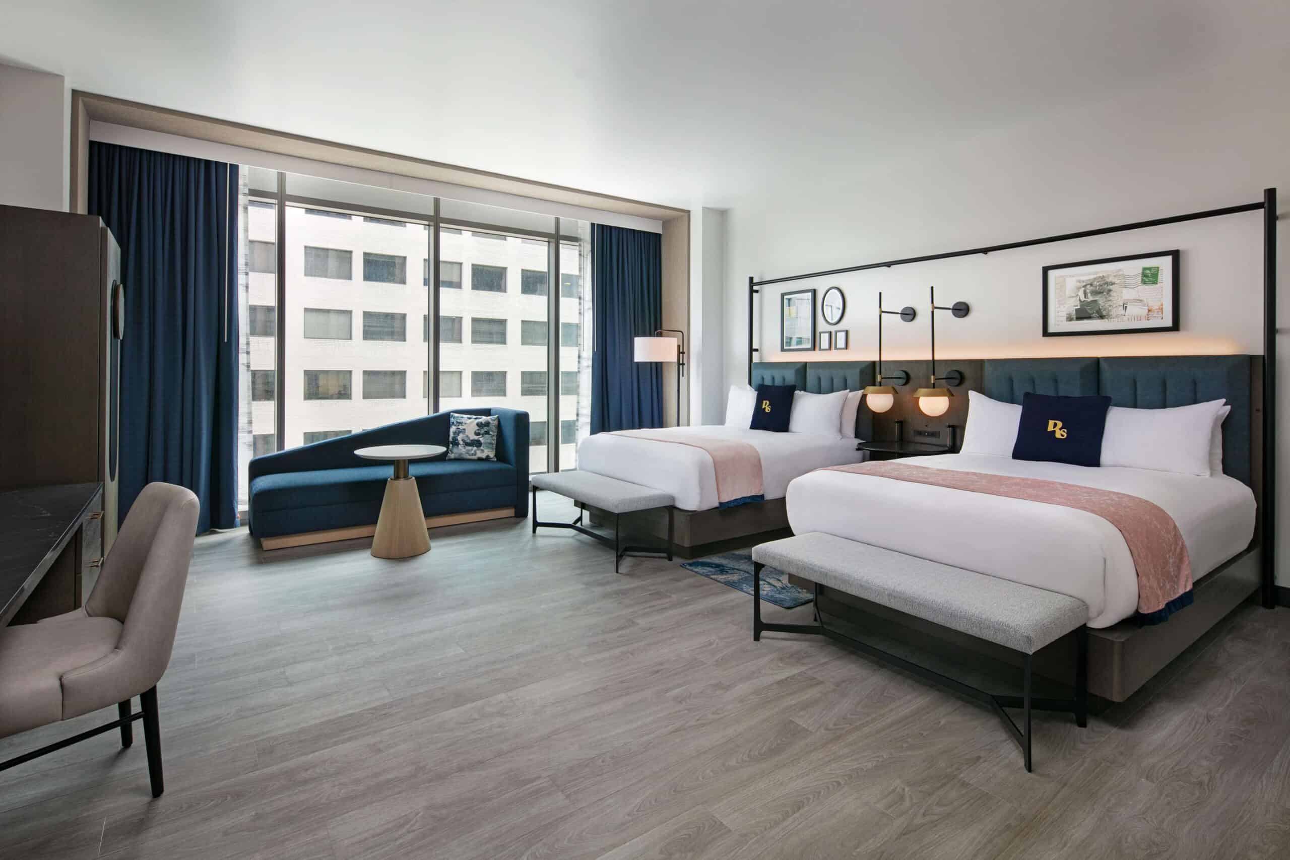 A room at The Royal Sonesta Capitol Hill featuring two beds, a pillow with a mascot design, large windows, and a view of the city outside.