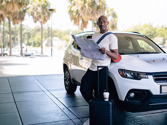 Guest standing beside a white SUV with luggage and a map outside the hotel entrance.