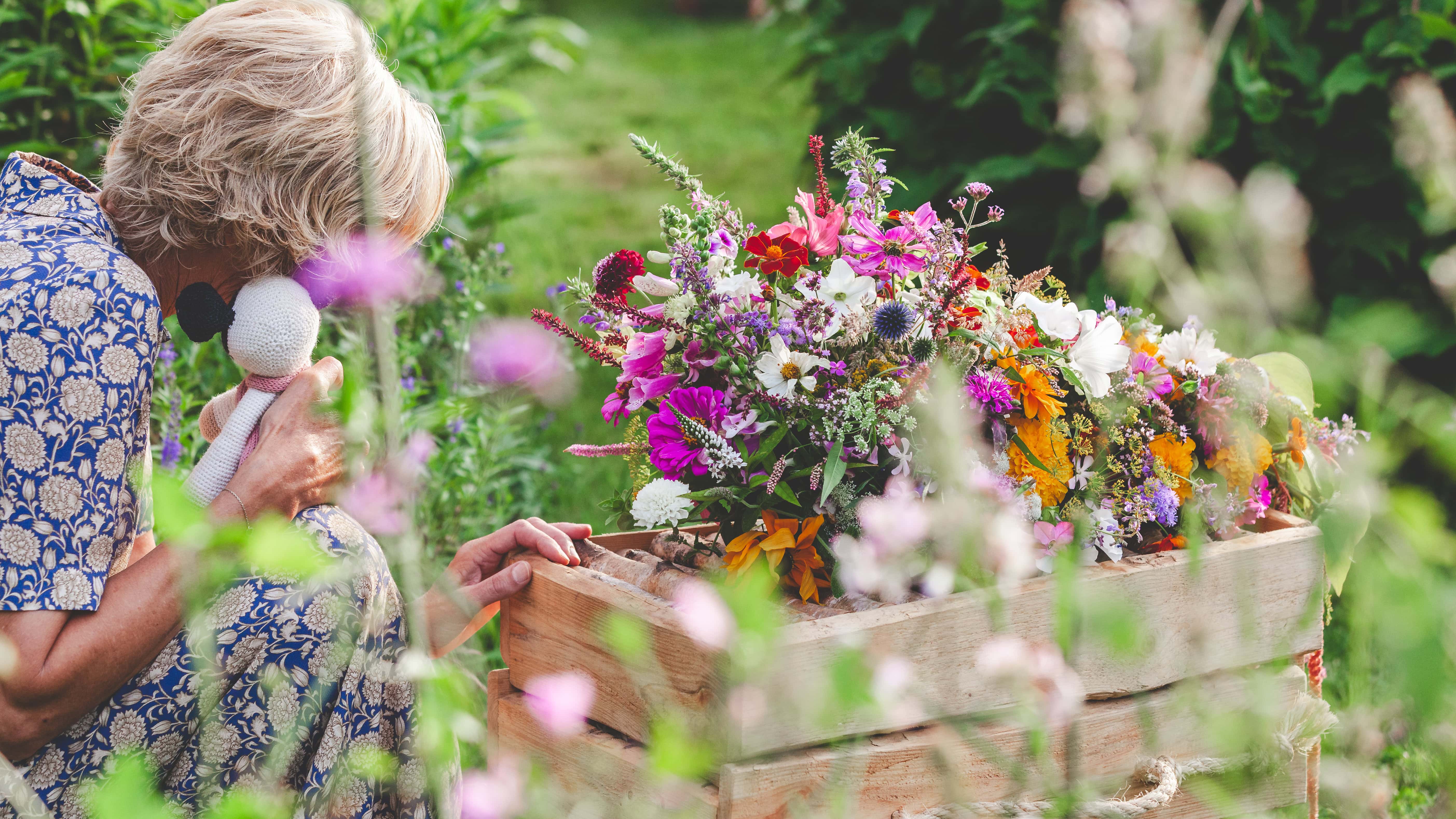 Uitvaartfotografie van een emotioneel moment waarbij een vrouw een knuffel vasthoudt terwijl ze haar hand op een kinderkistje legt