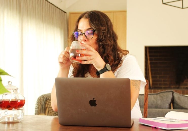 A woman drinks a cup of rooibos tea while working on her laptop