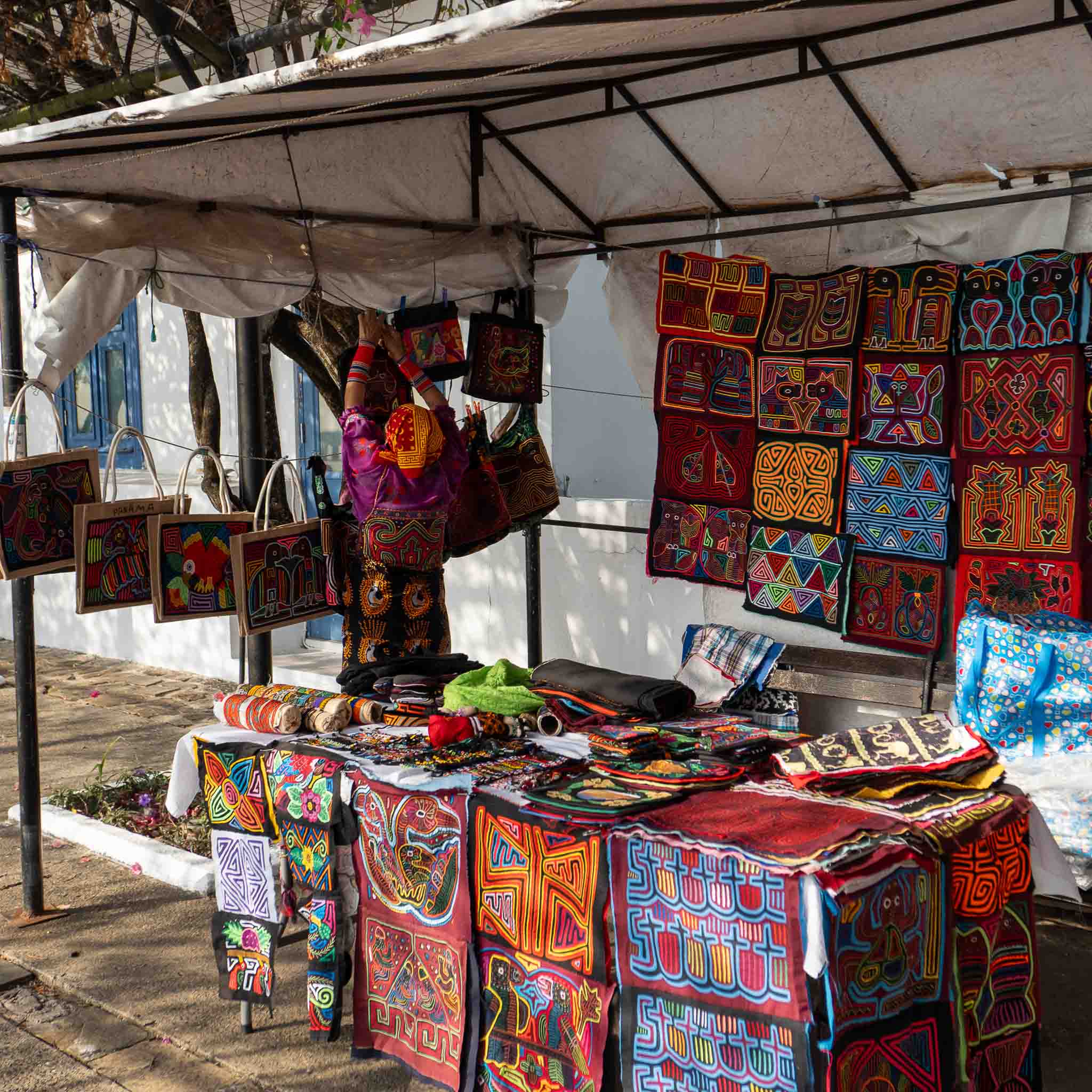 Kuna woman adjusting hand-sewn molas at a colorful artisan street stall in Casco Viejo, Panama