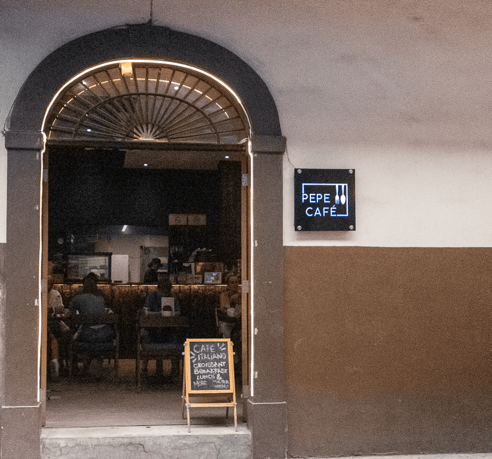 Entrance to Pepe Café in Casco Viejo with glowing archway, chalkboard sign, and diners seated inside.