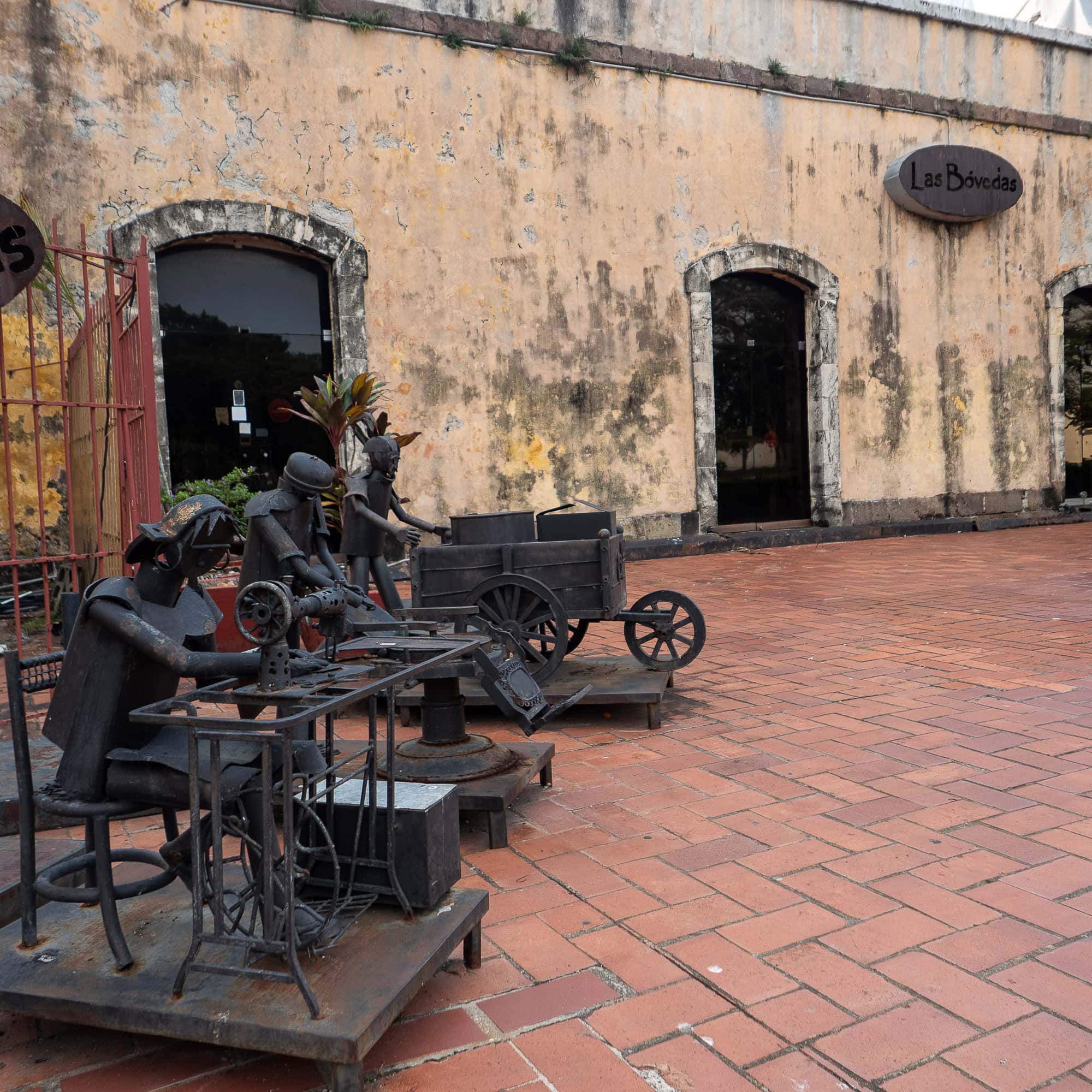 Metal sculpture of a street vendor pushing a cart, displayed on red tile at a cultural plaza in Casco Viejo, Panama.