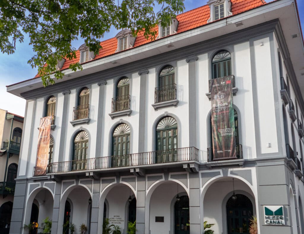 Front view of Museo del Canal Interoceánico in Casco Viejo, Panama, with colonial arches, tall green windows, and cultural banners on display. New Panama Canal Museum Renovation