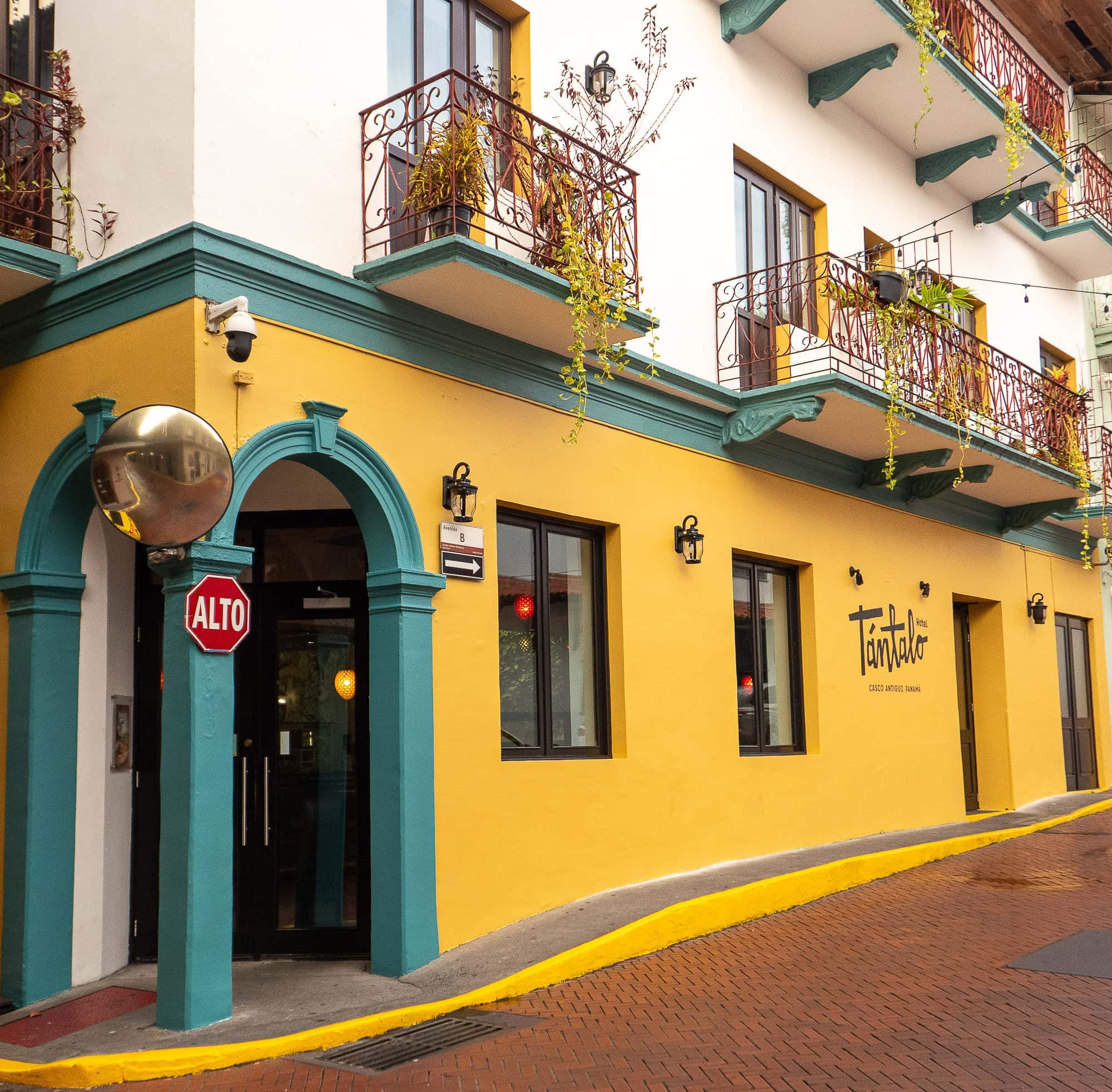 Corner view of Tántalo Hotel and Restaurant in Casco Antiguo, Panama, featuring vibrant yellow walls, teal trim, wrought-iron balconies, and a red ALTO sign.