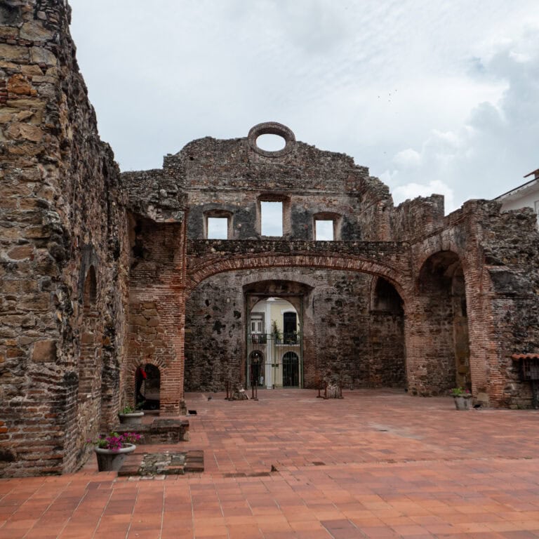 View from inside the Flat Arch ruins in Casco Viejo, showing arched stone walls and a gated entrance framing a colonial building across the street.