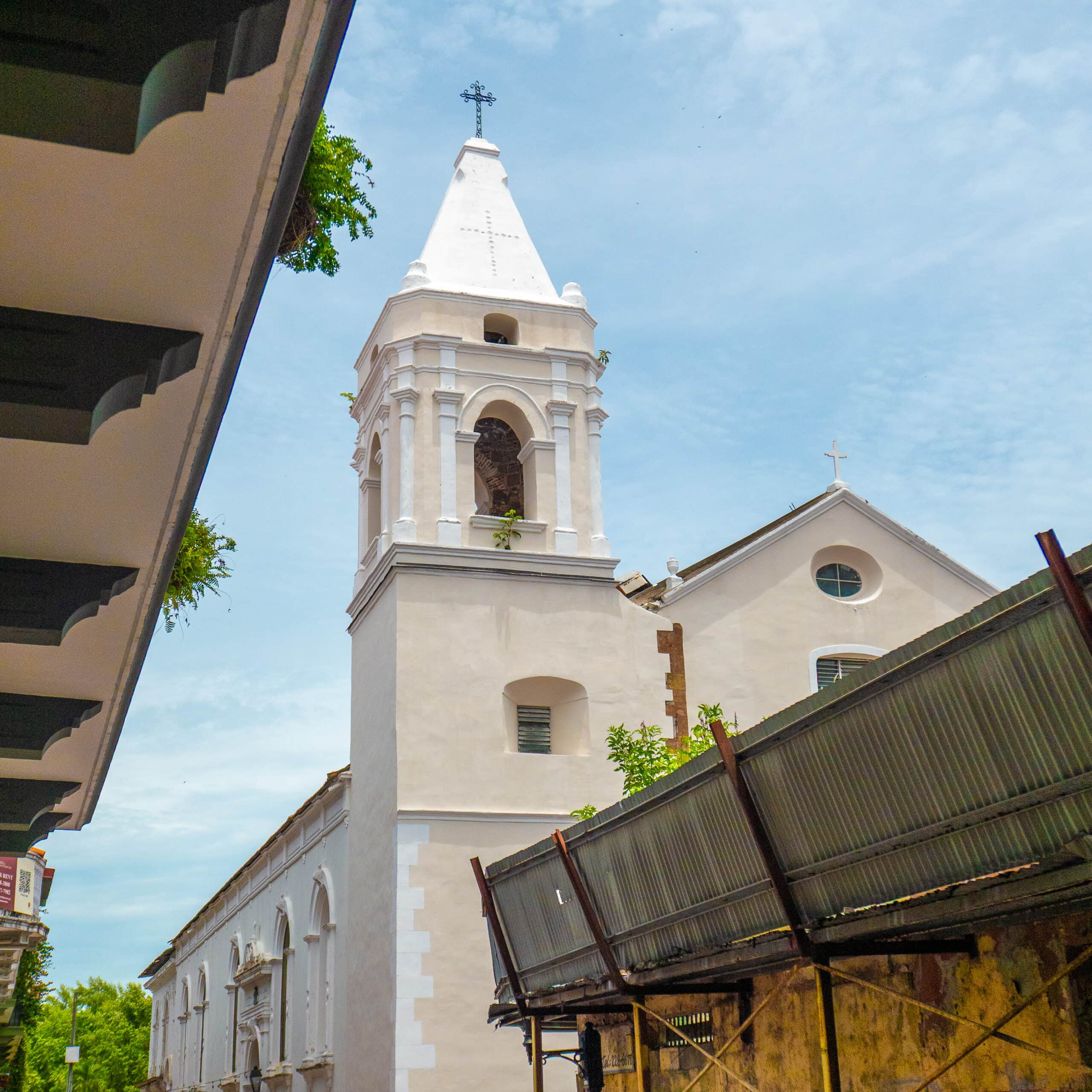 Colonial church tower in Casco Viejo with white bell tower and side construction, viewed from a narrow street.