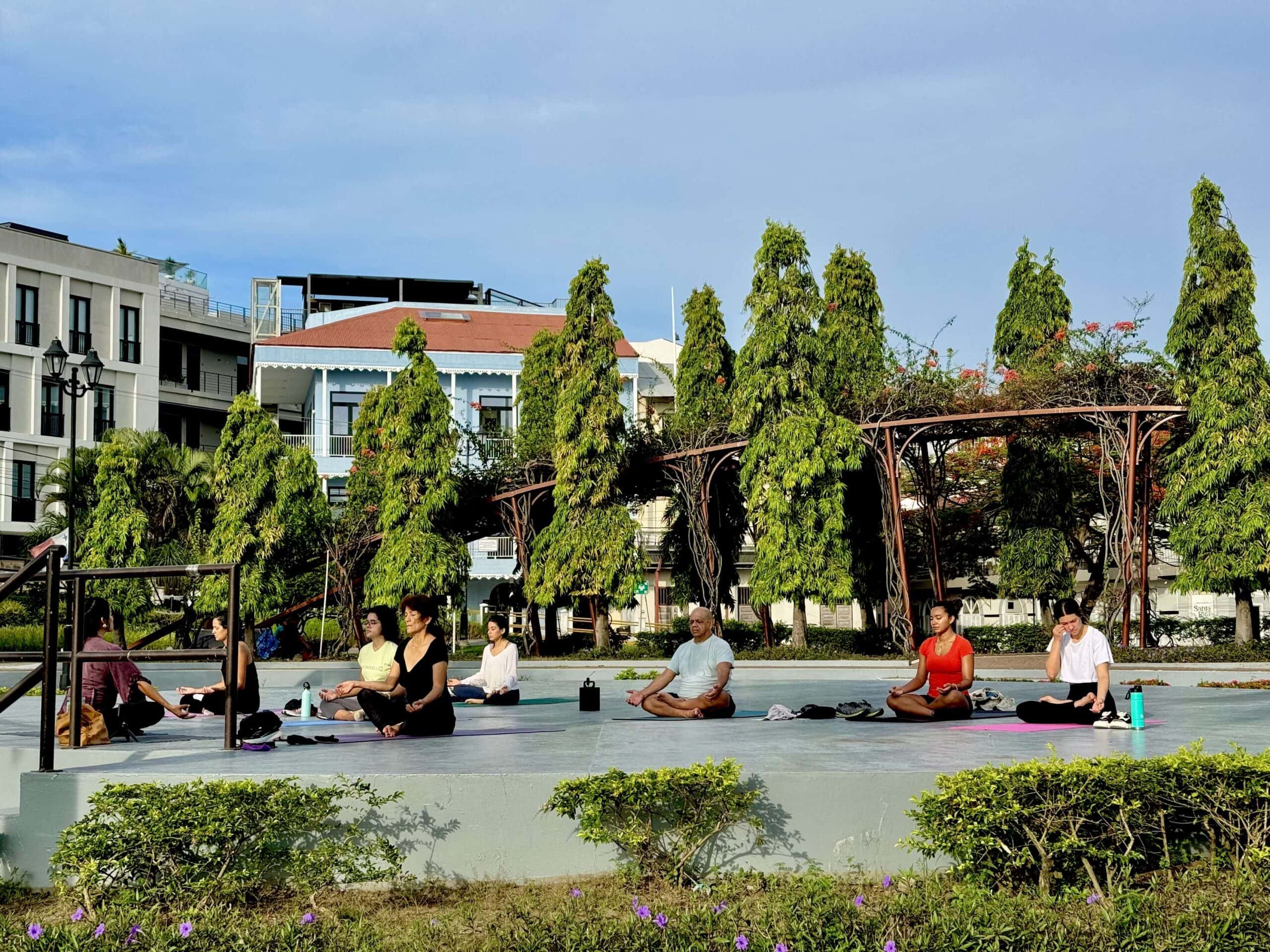 Group practicing morning yoga outdoors in a city park surrounded by trees and buildings