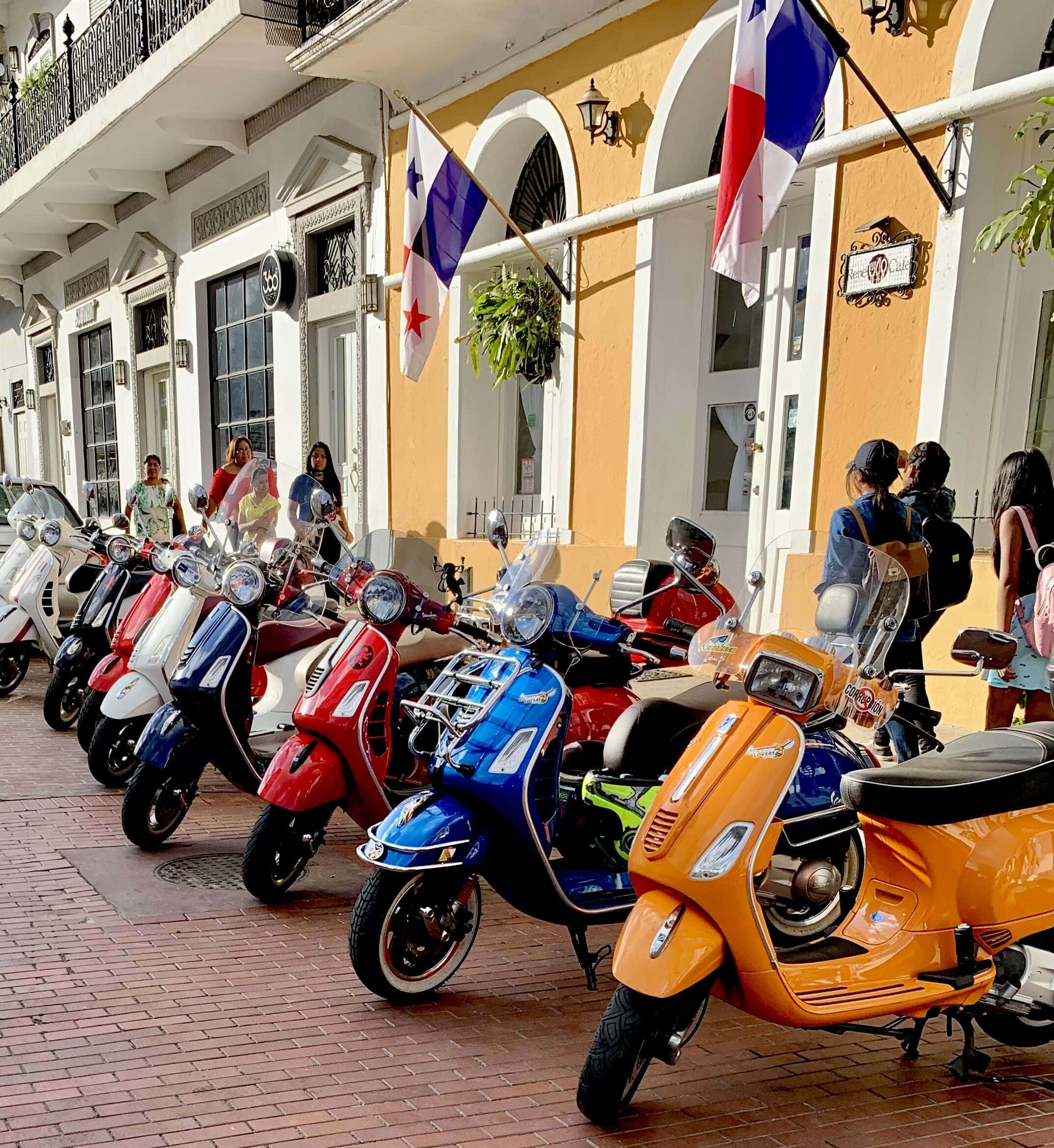 Colorful Vespa scooters parked along a historic street in Casco Viejo, Panama, with Panamanian flags above.