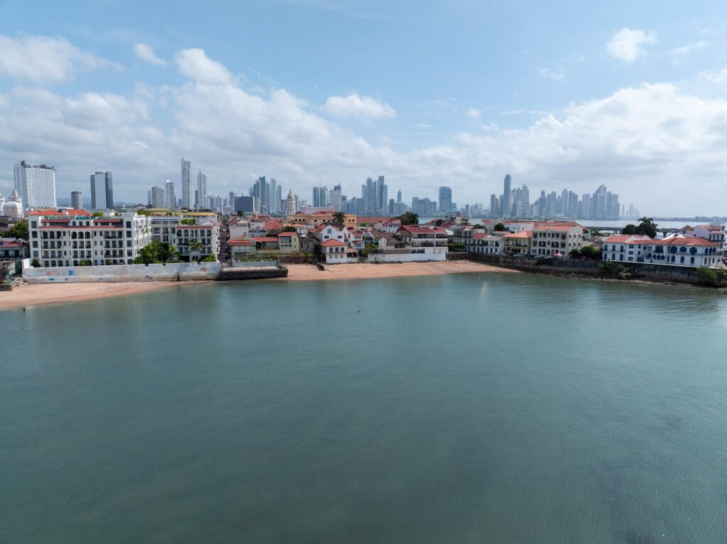 Panoramic daytime view of Casco Viejo with restored colonial buildings along the waterfront and the modern Panama City skyline in the background.