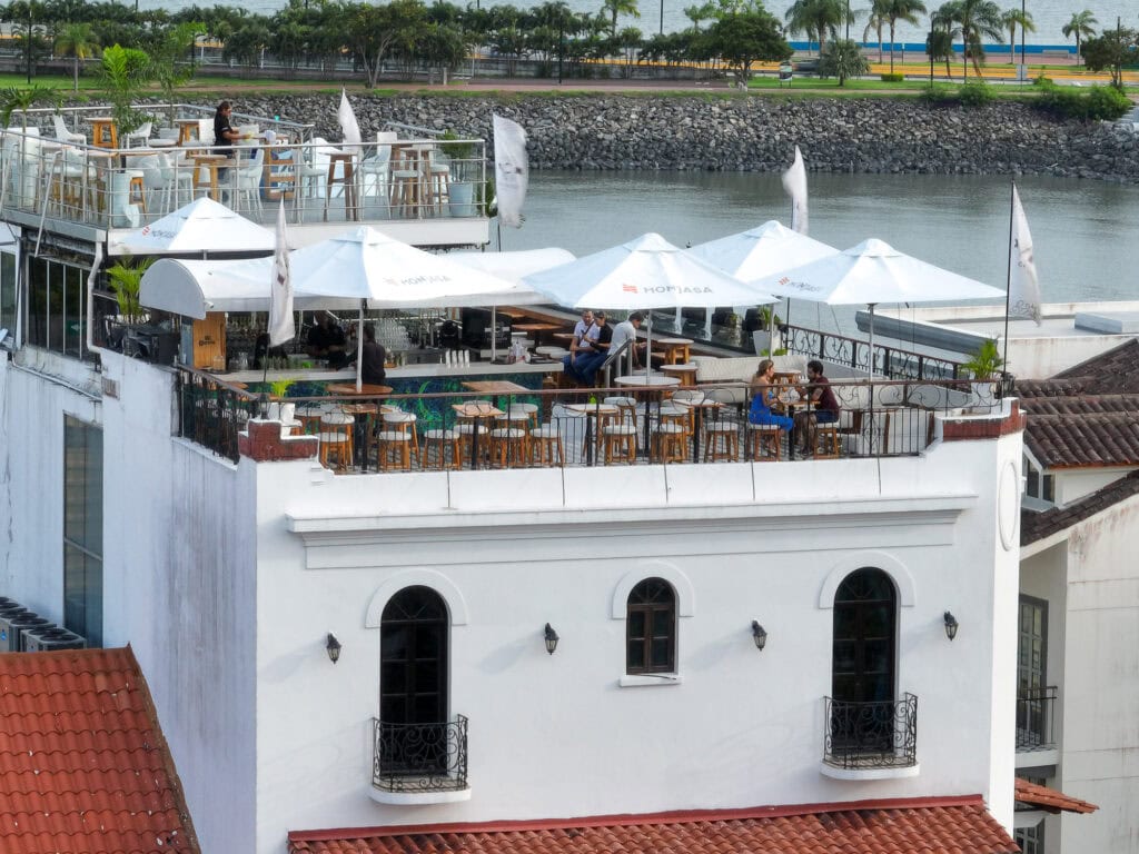 Aerial view of the CasaCasco Rooftop Bar in Casco Viejo, Panama, with outdoor seating, umbrellas, and views overlooking the Amador Causeway and waterfront.
