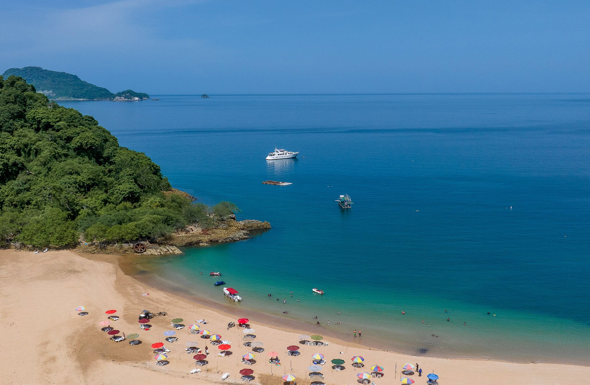 Colorful beach umbrellas line the sandy shore of Taboga Island as boats float in the clear blue waters nearby.
