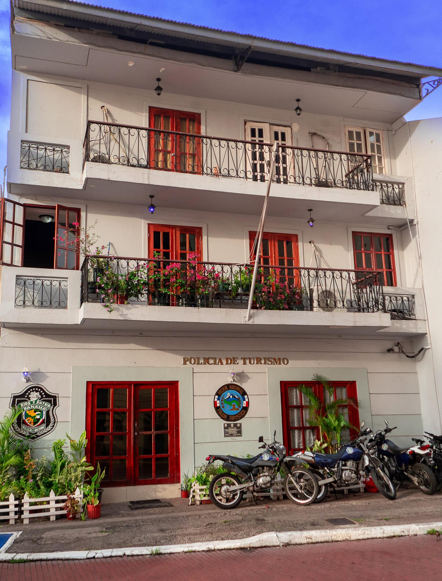 Tourist police station in Casco Viejo, Panama, with red balconies, potted plants, and parked motorcycles