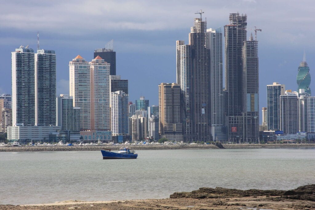 Panama City skyline viewed from Casco Viejo, with modern high-rise buildings rising along the coast and a fishing boat in the foreground.