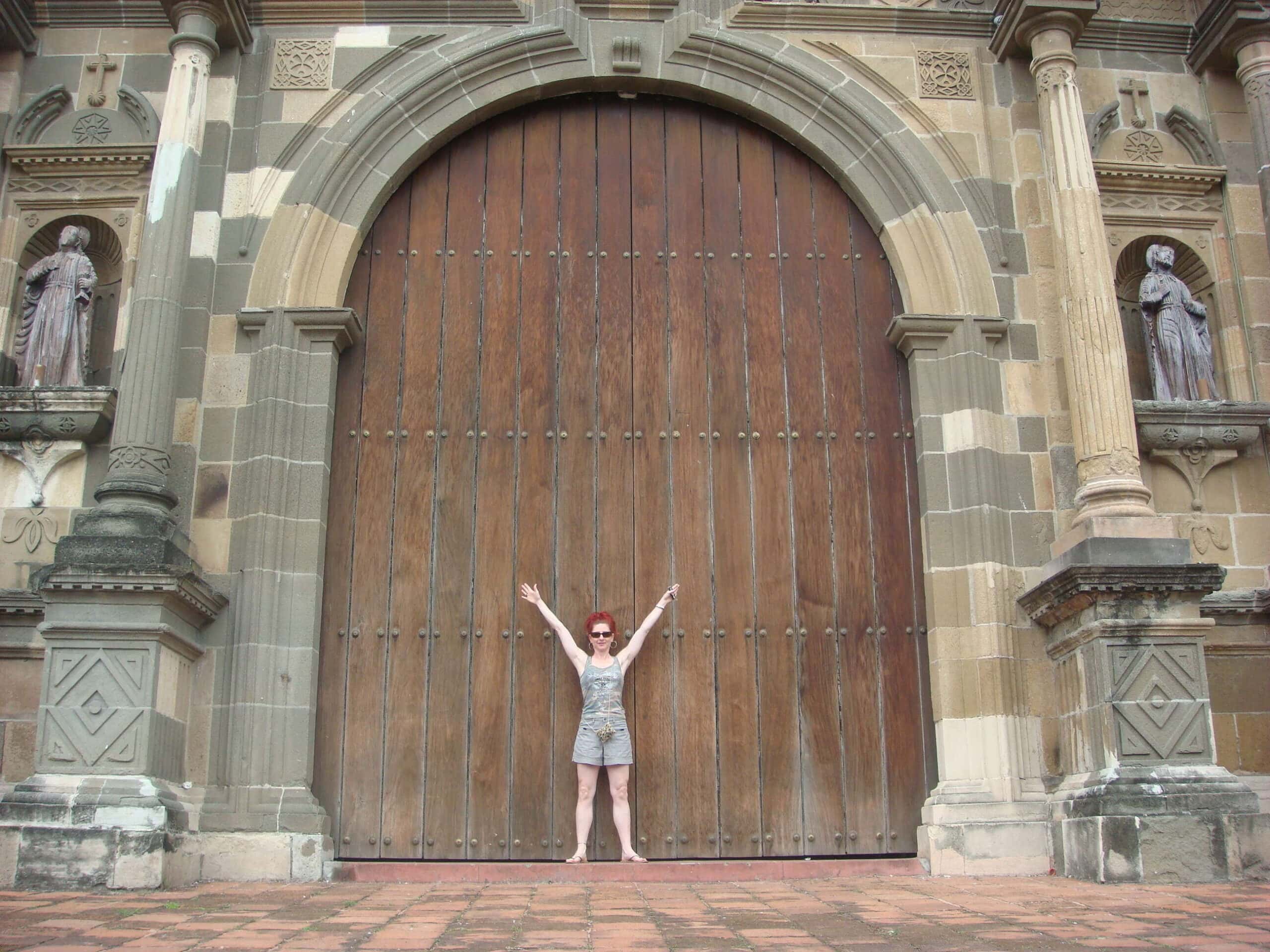 Tourist standing in front of the massive wooden doors of the Cathedral Basilica in Casco Viejo, arms raised in awe.