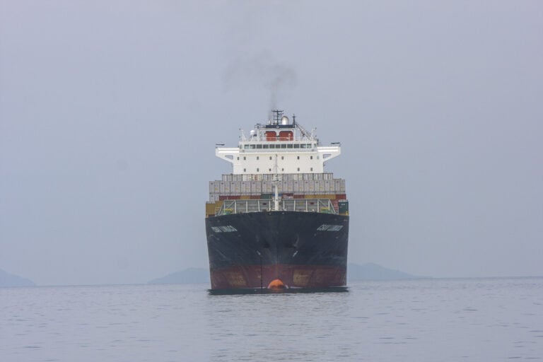 A large cargo ship heads directly toward the camera, preparing to enter the Panama Canal under overcast skies.