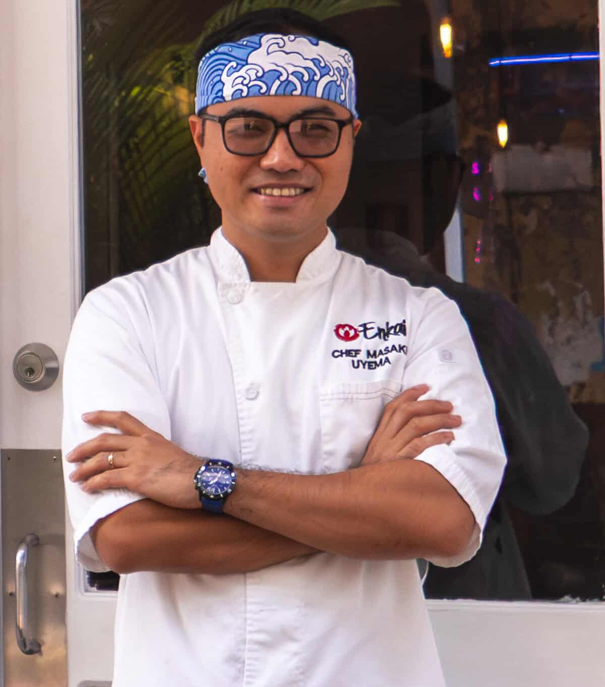 Chef Masaki Uyema standing outside Enkai Restaurant in Casco Viejo Panama wearing chef whites and a blue headband.