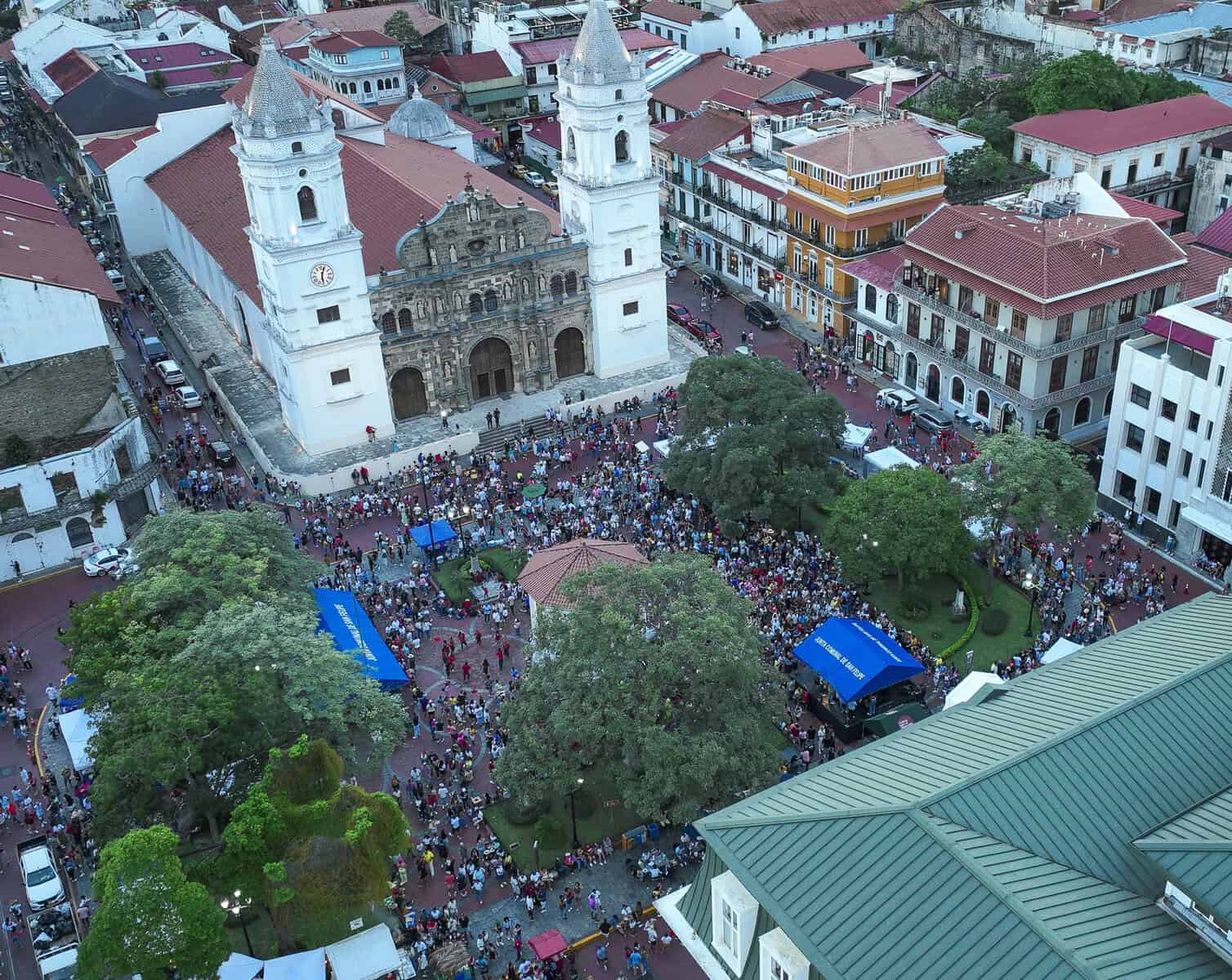 Aerial view of the Metropolitan Cathedral in Casco Viejo, Panama, during a public event with crowds filling Plaza de la Independencia.