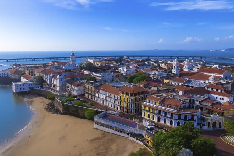 Aerial view of Casco Viejo Panama with bright blue sky and ocean backdrop, showing colonial buildings and the historic city center.