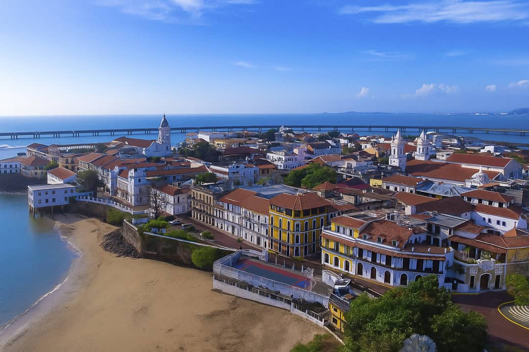 Aerial view of Casco Viejo Panama with bright blue sky and ocean backdrop, showing colonial buildings and the historic city center.