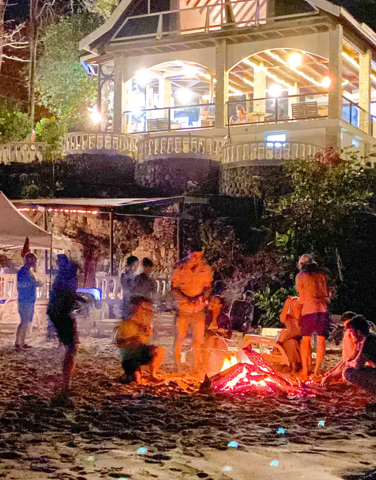 Evening beach gathering on Contadora Island with people around a bonfire and a lit pavilion overlooking the shoreline