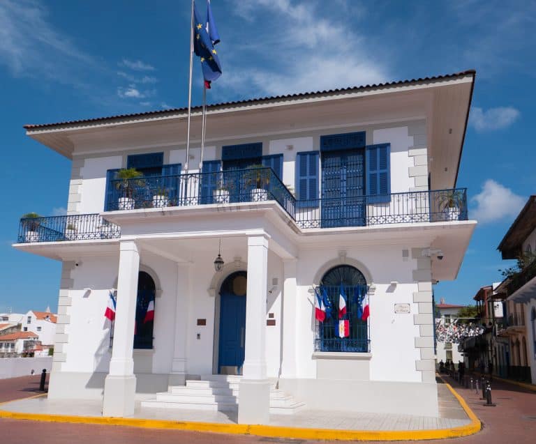 French Embassy building in Casco Viejo, Panama, with blue shutters, colonial architecture, and French flags displayed.