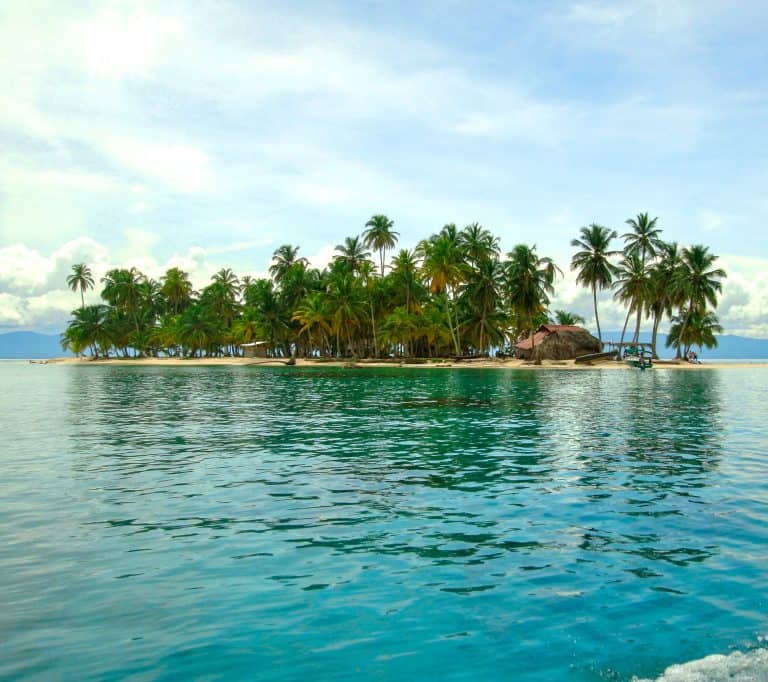 Palm-lined island in the San Blas Islands with turquoise water and traditional thatched hut