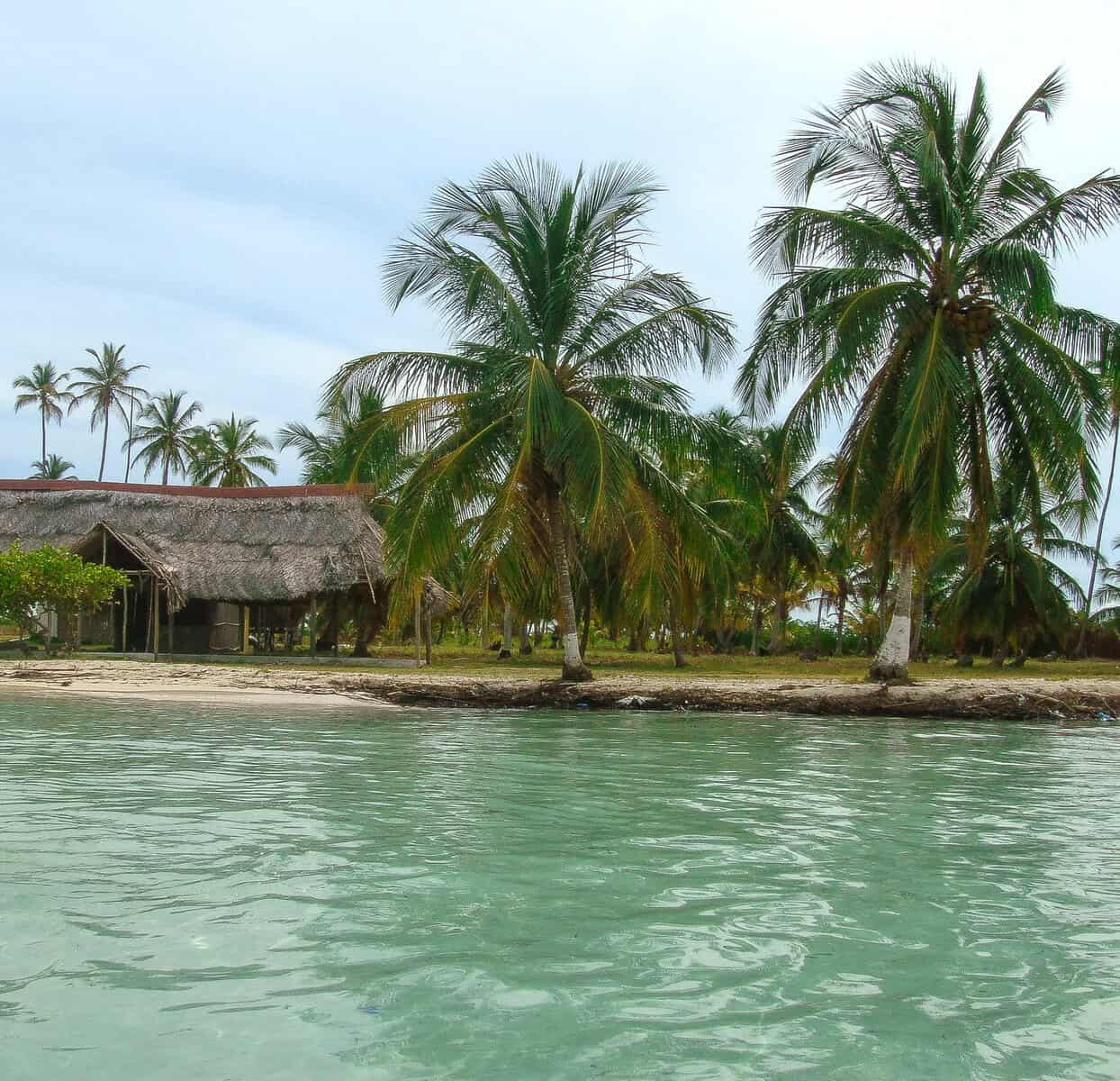 Palm-lined island in the San Blas Islands with turquoise water and traditional thatched hut