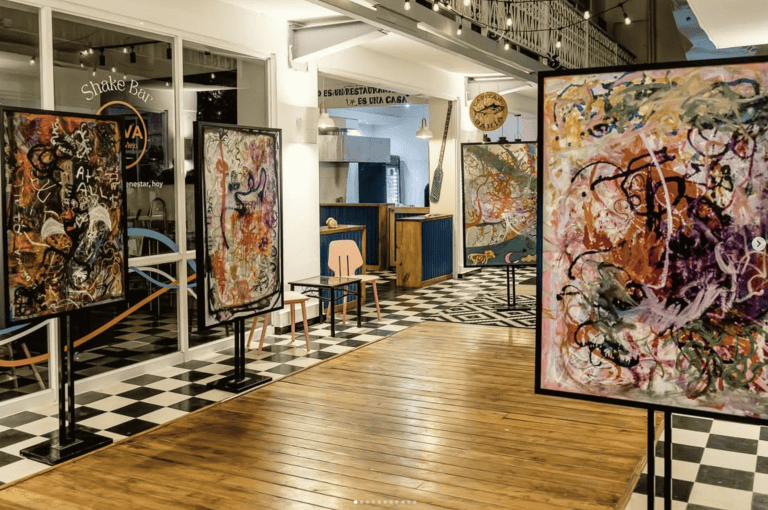 Arco Soleil art installation at Galería Solar Casco Viejo, with abstract paintings on display and checkered floors beneath string lights.