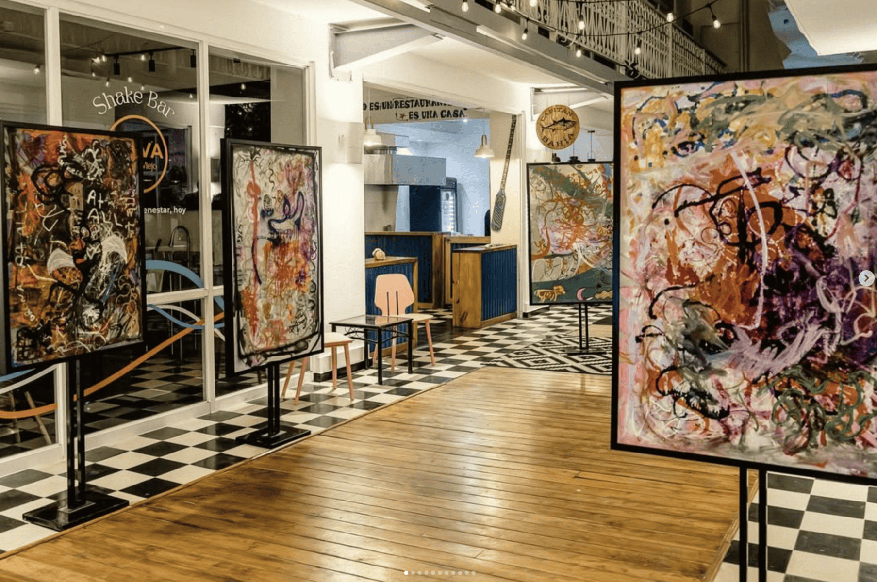 Arco Soleil art installation at Galería Solar Casco Viejo, with abstract paintings on display and checkered floors beneath string lights.