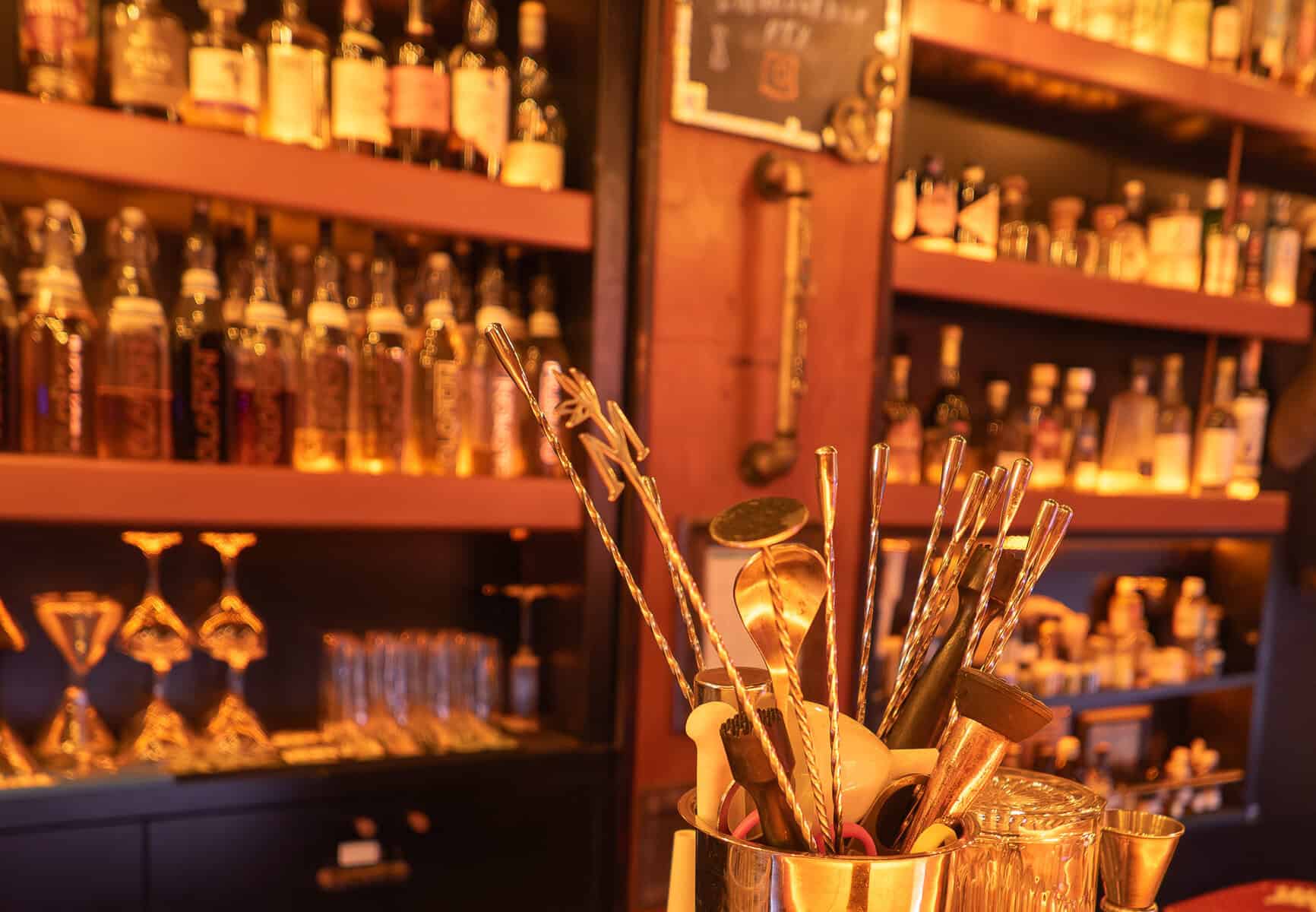Bar tools and cocktail-making equipment at Element Bar Casco Viejo, set against shelves of infused spirits inside the historic bar
