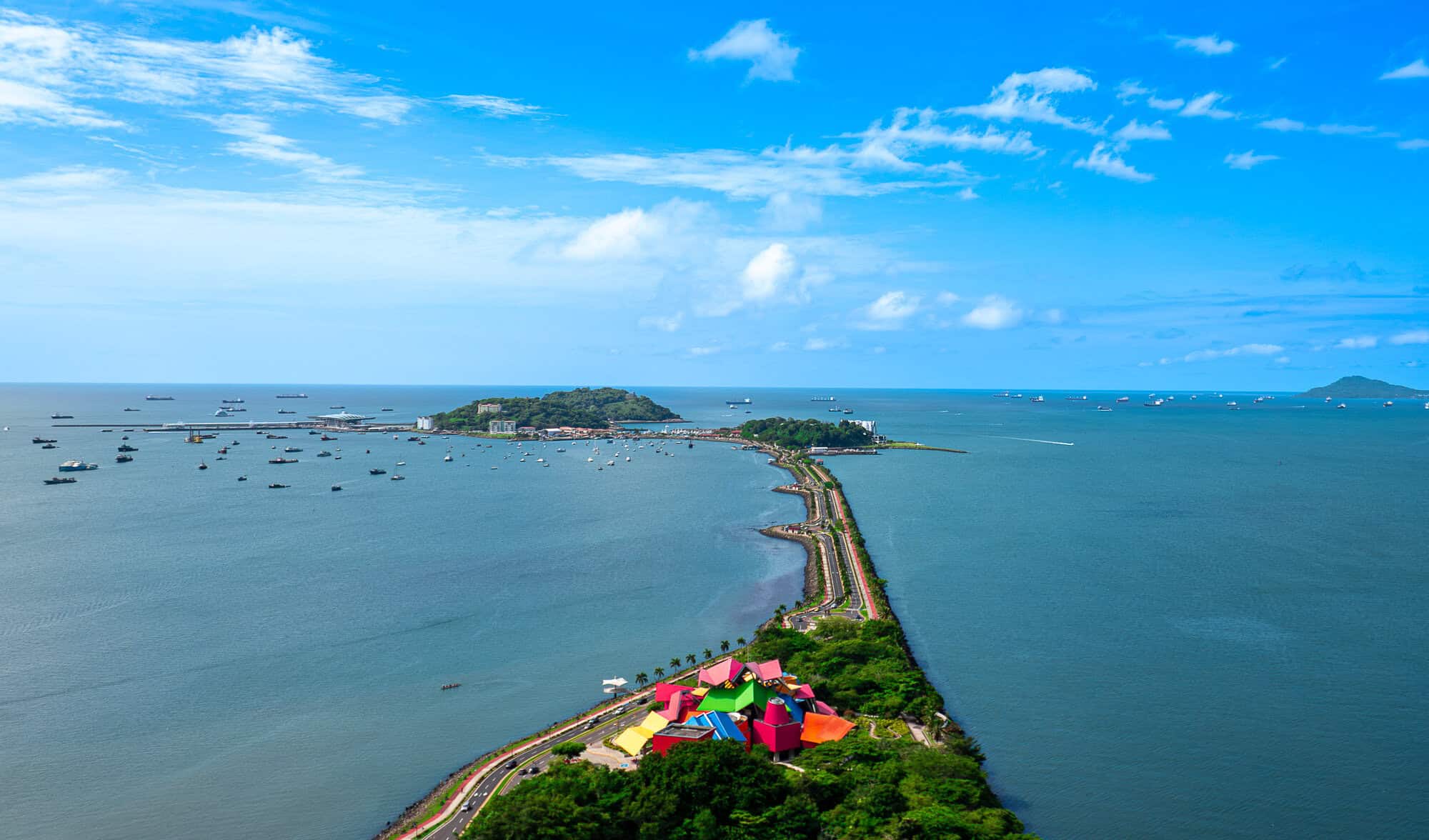 Aerial view of the Amador Causeway leading toward Naos, Perico and Flamenco Islands with the colorful Biomuseo and ships anchored in the Pacific Ocean near the Panama Canal.