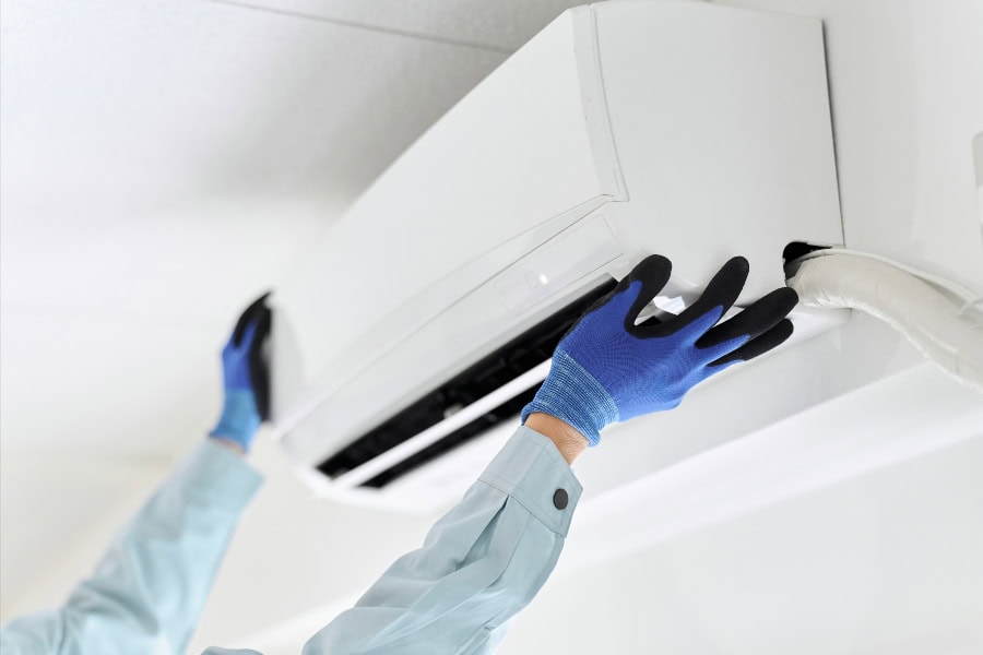Person opening the front panel of a wall-mounted air conditioner to access the filter for cleaning.