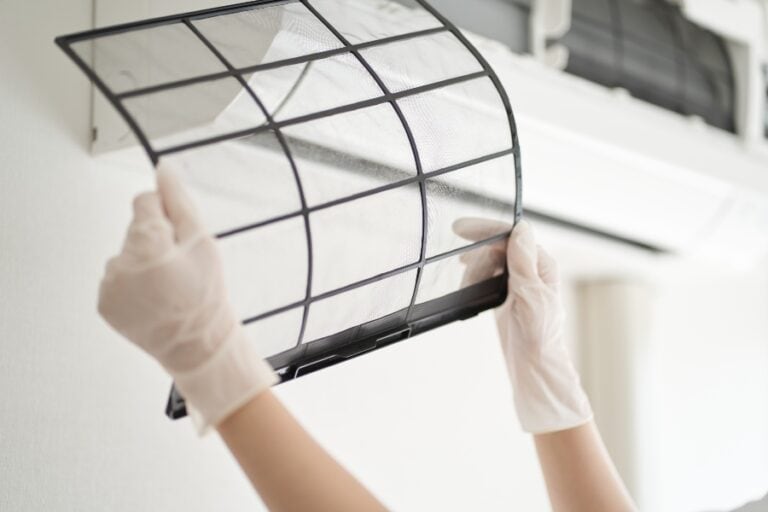 Person removing a dirty air conditioner filter for cleaning as part of regular AC maintenance in 2025.
