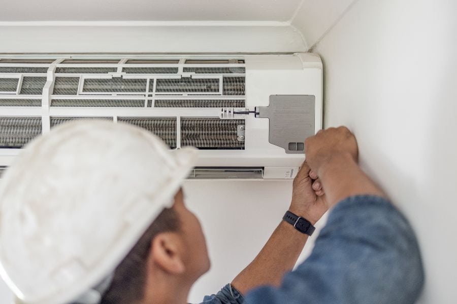 Technician repairing wall-mounted air conditioner unit to fix water leakage issue.