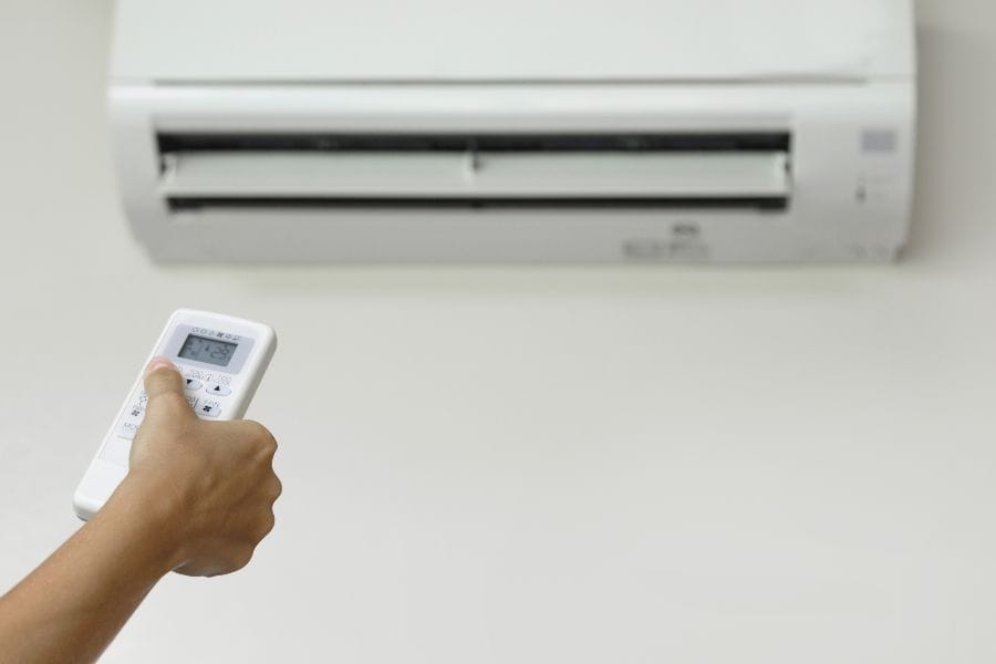 Hand holding remote to operate wall-mounted air conditioner, keeping room cool and dry.