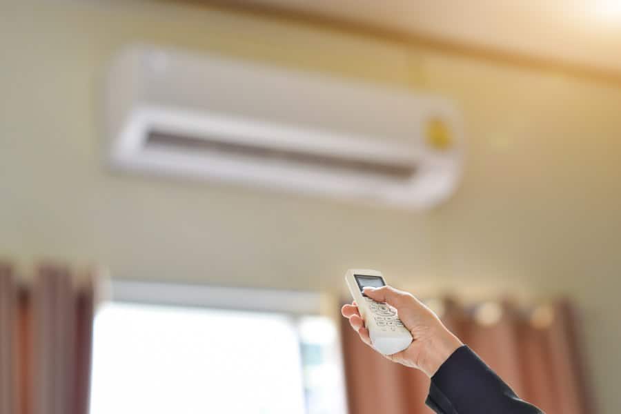 Hand using remote to control reverse cycle air conditioner for heating and cooling.
