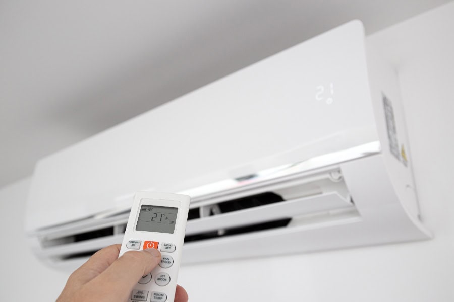 Person using a remote control to adjust temperature on a smart inverter air conditioner unit.