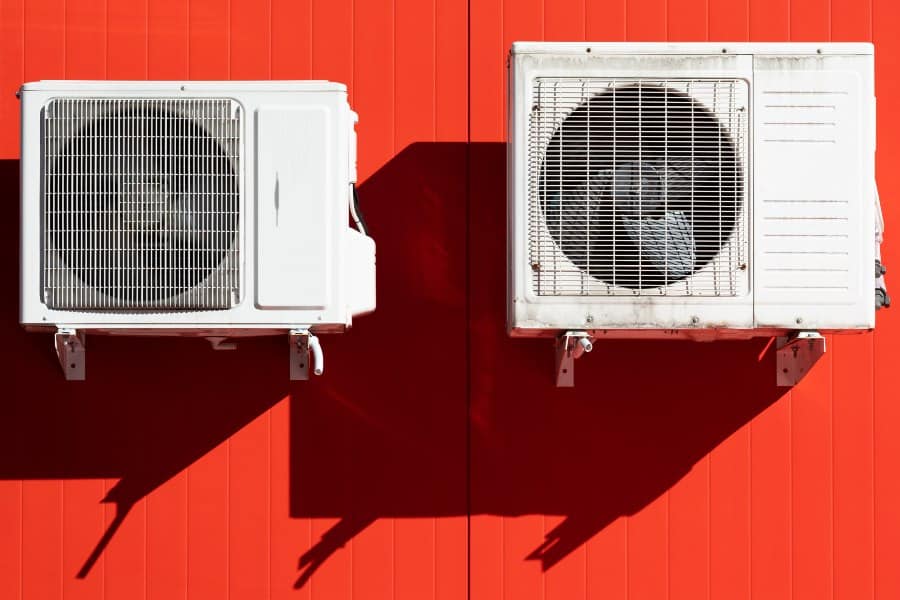 Two outdoor air conditioning units mounted on a bright red wall for climate control efficiency.