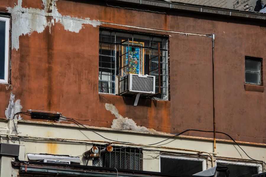 Window air conditioner unit installed on a window frame for single-room cooling.