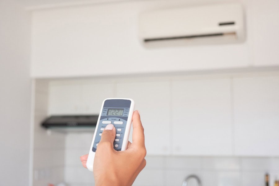 Hand holding remote to adjust a wall-mounted air conditioner in a modern kitchen.