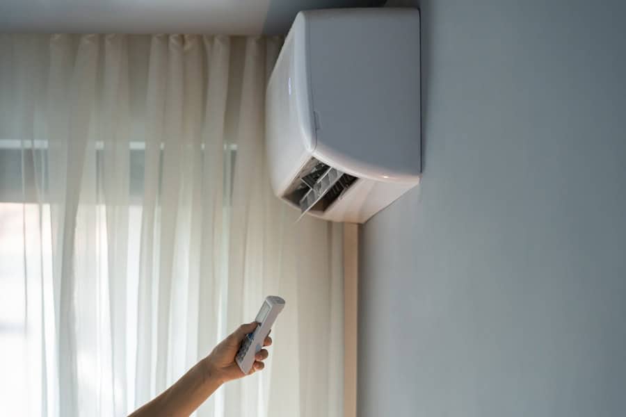 Person using a remote to control a modern wall-mounted air conditioning unit indoors.