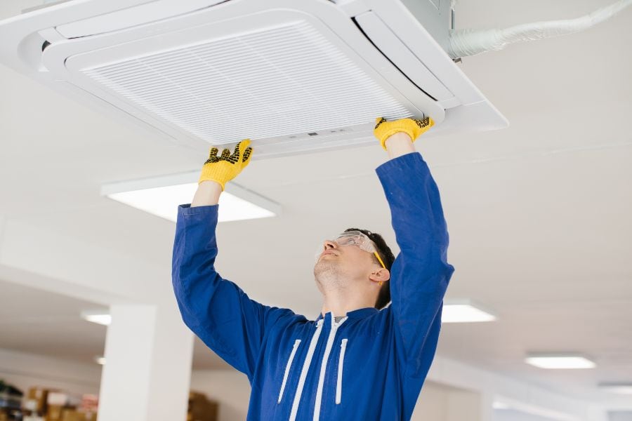 Technician installing a ceiling-mounted air conditioning cassette unit.